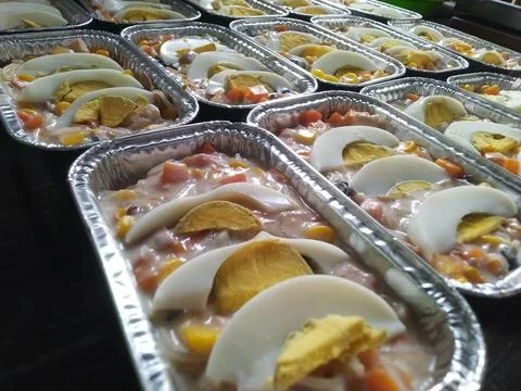 Rows of prepared creamy salad featuring sliced boiled eggs in foil containers Stock Photos