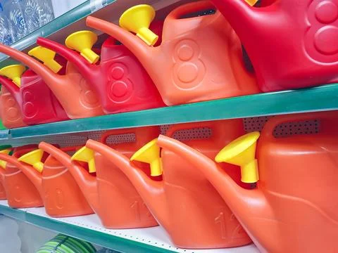 Rows of red and orange plastic watering cans with yellow spouts on store sh.. Foto stock