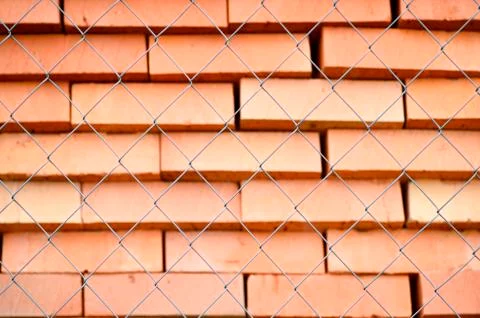 Rows of red bricks ready for transport over the wire fence of the store. Back Stock Photos
