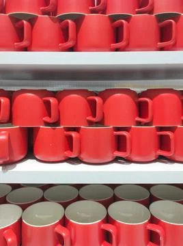 Rows of red ceramic mugs neatly arranged on shelves. Stock Photos