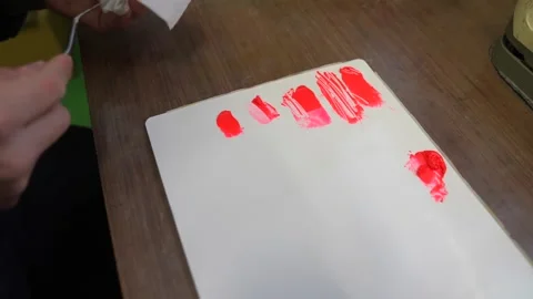 Rows of red paint swatches drawn on a white test card as a technician adds 動画素材 347123977