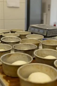 Rows of round baking pans holding proofing dough on wooden trays in bakery shop Stock Photos
