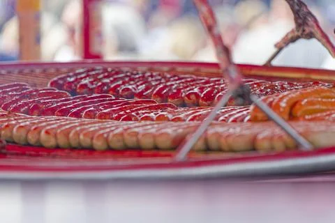 Rows of sausages grilling on a large round barbecue grill at an outdoor event Stock Photos