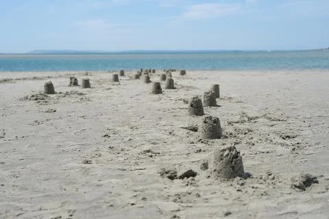 Rows of Small Sandcastles on a Sandy Beach Leading to the Ocean Stock Photos