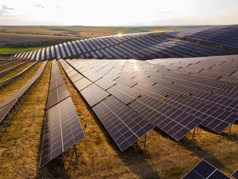 Rows of solar panels are arranged on a gently sloping field. The sun sets in  Stock Photos