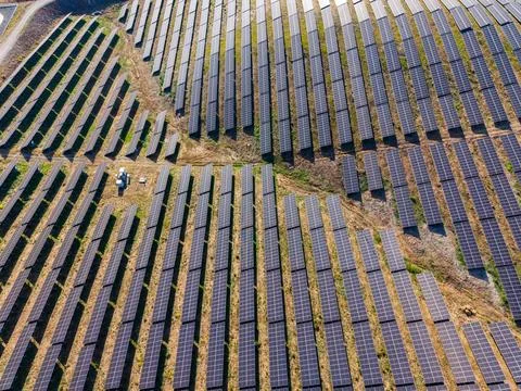 Rows of solar panels are arranged in a grid pattern across the fields. Worker Foto stock