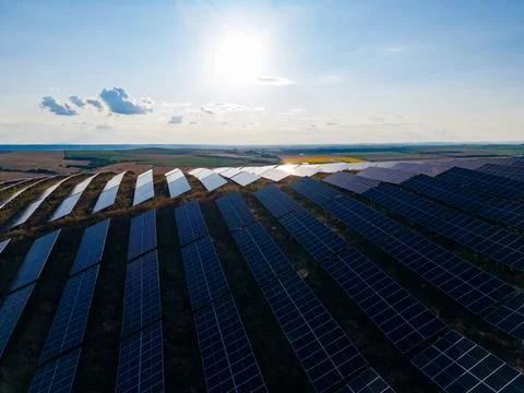 Rows of solar panels are set up in a wide field next to a water body. The sun Stock Photos