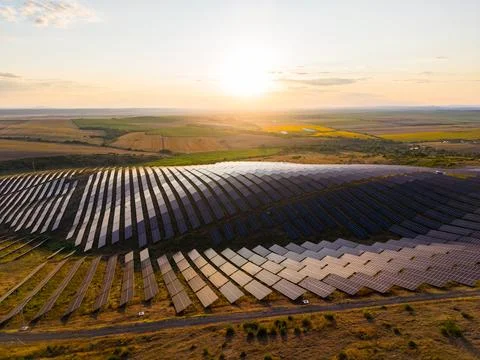 Rows of solar panels cover large fields as the sun sets. The landscape shows  Stock-Fotos