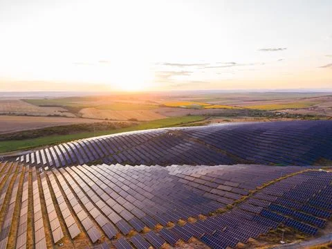 Rows of solar panels reflect light as the sun sets over fields in a rural loc Stock-Fotos