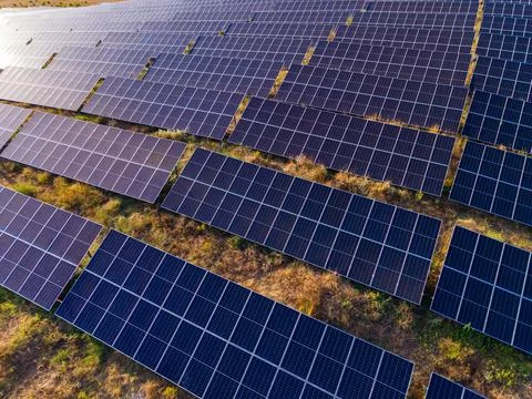 Rows of solar panels spread across a field in a sunny area, connected to a fa Stock Photos