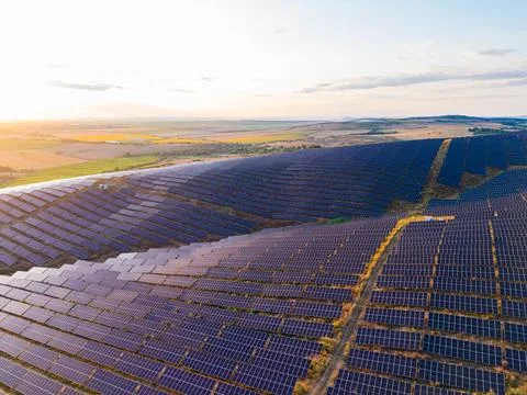 Rows of solar panels stretch across a vast field in a rural area. The sun set Stock Photos