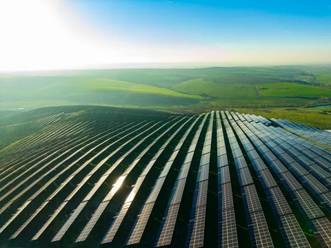 Rows of solar panels stretch across rolling hills under a clear sky. Green fi Stock Photos