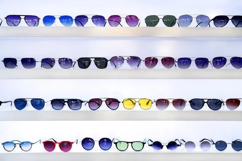 Rows of sunglasses in various styles and colors on white shelves, showcasin.. Stock Photos