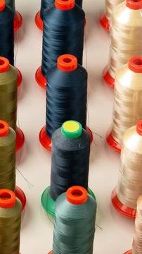 Rows of thread spools in various colors on a flat surface in a crafting area Stock Photos