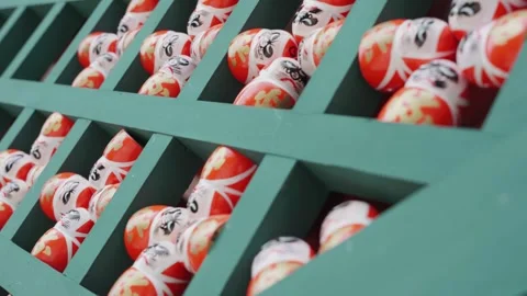 Rows of traditional Daruma dolls are arranged on green wooden shelves at Stock Footage 344278819