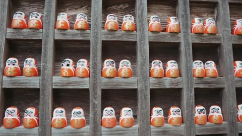 Rows of traditional Daruma dolls are arranged on rustic wooden shelves at Stock Footage 344280329