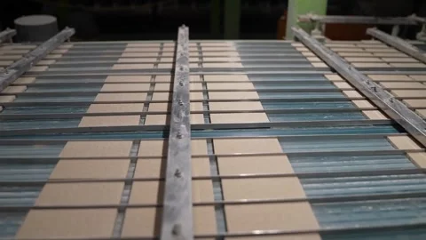 Rows of unfired tan ceramic tiles travel on a slatted conveyor beneath an Vídeo Stock 346737912