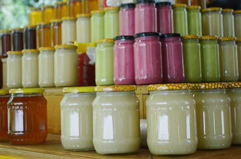 Rows of various jars of honey and berry jam on wooden shelves in a market sta Stock Photos