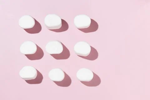 Rows of white marshmallows pattern on light pink table background in hard lig Stock Photos