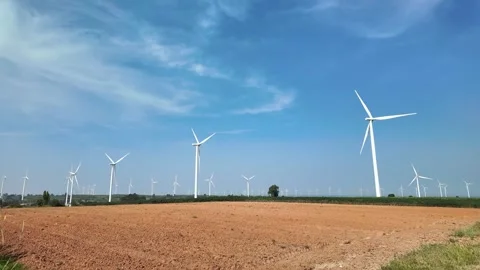 Rows of wind turbines stand tall across open farmland beneath a bright blue sky 스톡 동영상 314817294