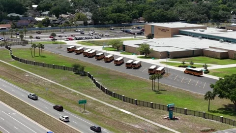 Rows of yellow school buses line pavement outside high school campus in Plant 库存影片 340968849