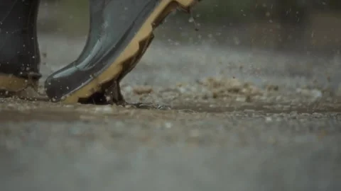 Rubber boots step on a puddle and creates a splash which flies around. Slow Stock Footage 313283657