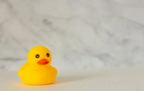 Rubber duck on a marble background with a copy of the space. Stock Photos