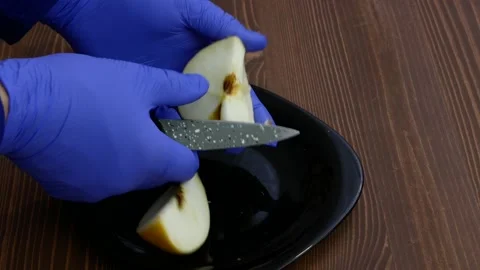 Rubber-gloved hands cut a piece of apple in half. Stock Footage 153236363