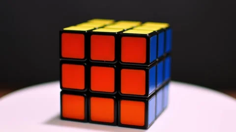 A Rubik's cube is rotating on a white surface against a black background. Stock Footage 303354336