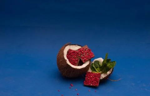 Ruby chocolate pieces inside of half coconut decorated with basil. blue backg Stock Photos