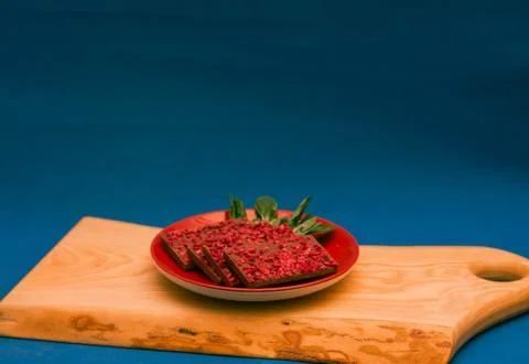 Ruby chocolate pieces on red plate on wooden chopping board. Blue background Stock Photos