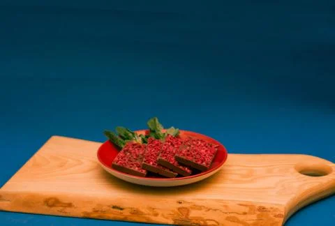 Ruby chocolate pieces on red plate on wooden chopping board. Blue background Stock Photos
