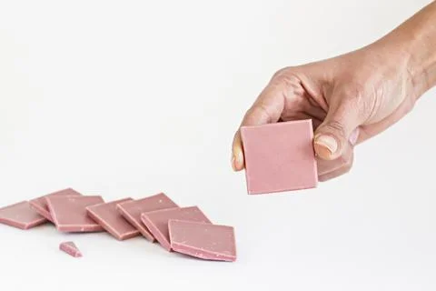 Ruby chocolate sliced and hand holding one piece on white Stock Photos