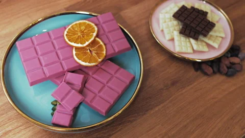 Ruby dark and white chocolate bars with orange slices and cacao seeds on a table Video stock 239306105