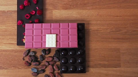 Ruby dark and white chocolate bars on a wooden table with cocoa seeds - Top view Video stock 239681532