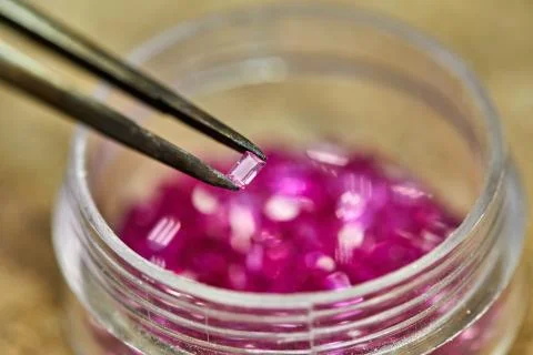 Ruby held by tweezers on the background of rubies in the bo 스톡 사진