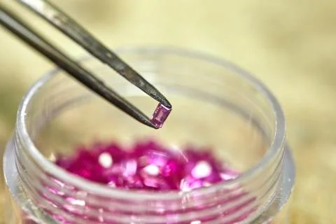Ruby held by tweezers on the background of rubies in the bo Foto stock