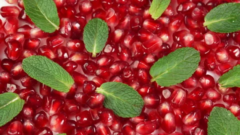 Ruby pomegranate seeds with green mint leaves rotate as background showcase. Red Stock Footage 307810039