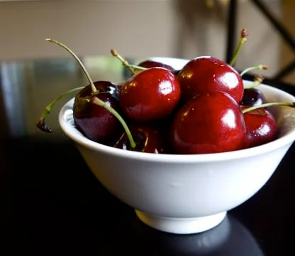 Ruby red cherries in white bowl on black table Stock Photos