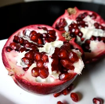 Ruby red, pomegranate, halved on white plate - black table Stock Photos