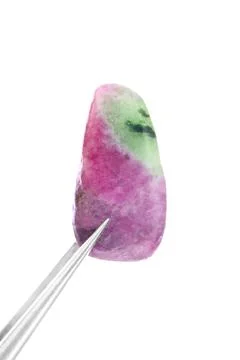 Ruby zoisite jewel stone texture in tweezers on light surface background. Mac Stock Photos