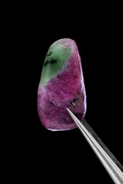 Ruby zoisite jewel stone texture in tweezers on black background. Macro close Stock Photos