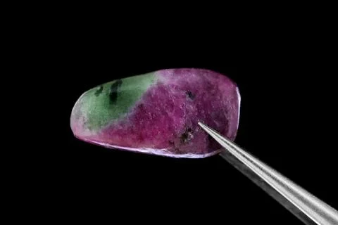 Ruby zoisite jewel stone texture in tweezers on black background. Macro close Stock Photos