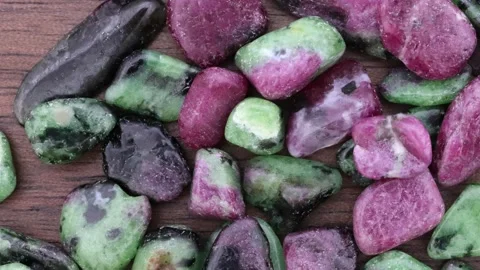 Ruby zoisite jewel stones heap up texture on brown varnished wood background. Stock Footage 221103314