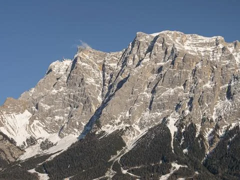 Rugged alpine cliffs with snowy summit and forested slopes in bright daylight Photos