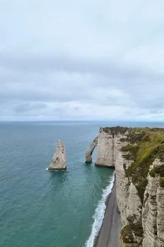 Rugged cliffs of Etretat rising dramatically from the azure sea, bordered by  Stock Photos