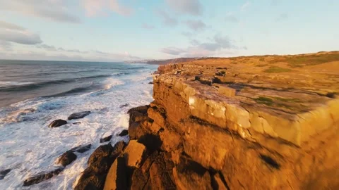 Rugged cliffs meet crashing waves under golden dusk light Video stock 340914599