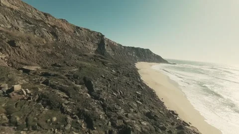Rugged cliffs meet soft, sunlit sand Stock Footage 341824650