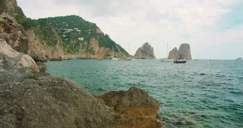 Rugged cliffs overlook turquoise sea with distant Faraglioni rock stacks Capri Video stock 327756129