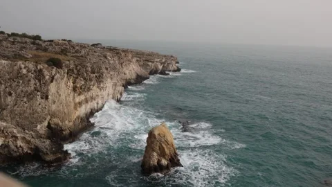 Rugged cliffs with waves crashing against a lone coastal rock Stock Footage 328286912